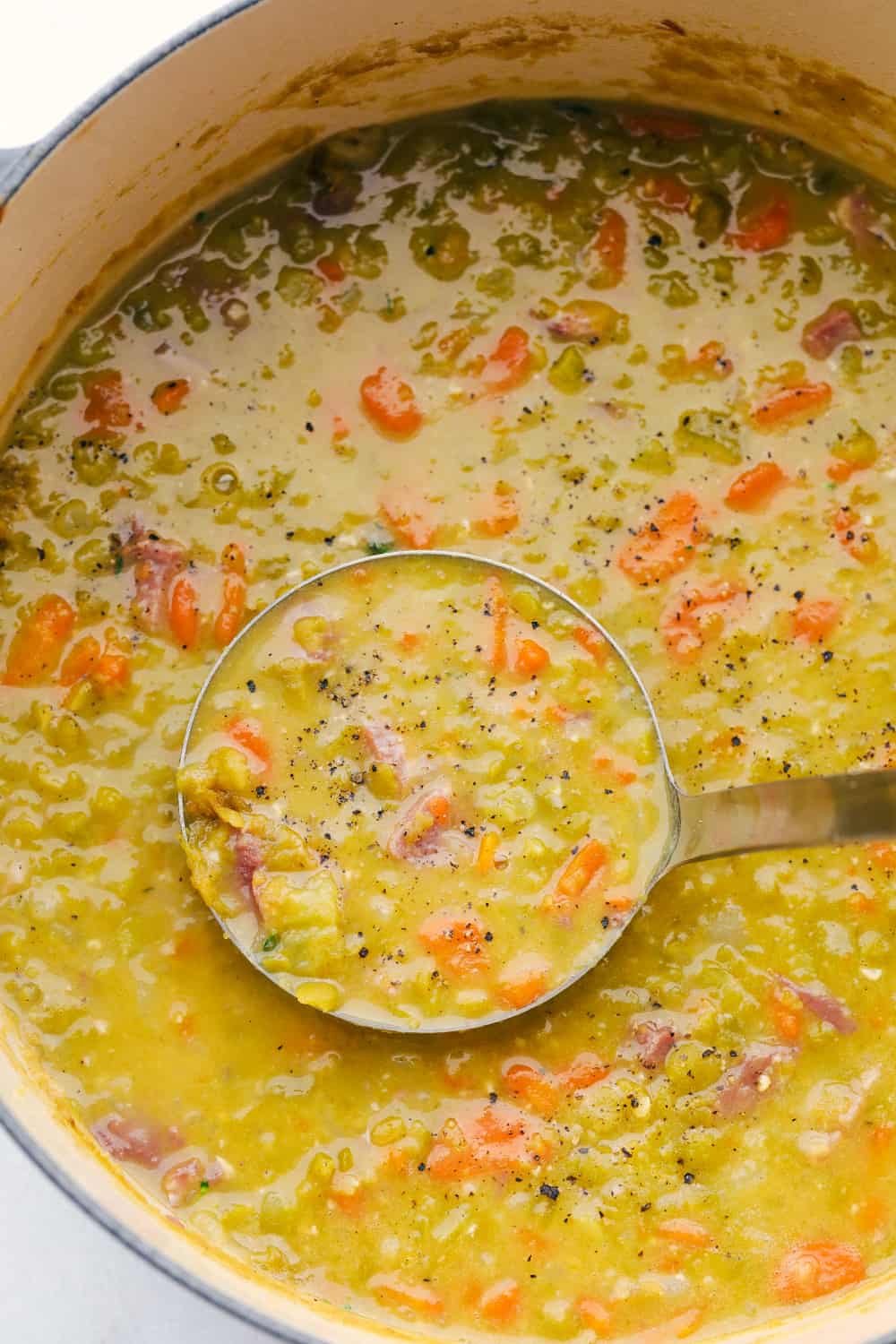 Split Pea Soup with ham is the perfect comfort food for any occasion. Full of vegetables, flavored with ham and cooked to perfection, you and your family are going to LOVE this soup. Ladling split pea soup out of stock pot.