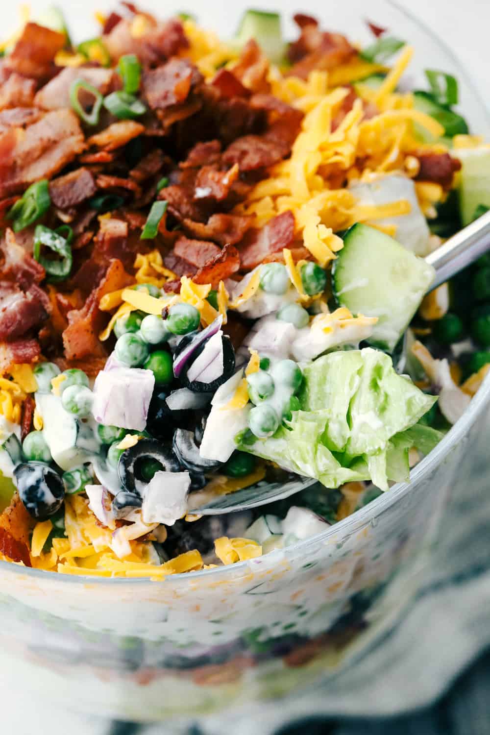 7 Layer Salad is super simple, customizable and amazingly delicious. This sensational traditional salad is a table topper as well as a scrumptious side dish. Scooping the 7 layer salad with a spoon.