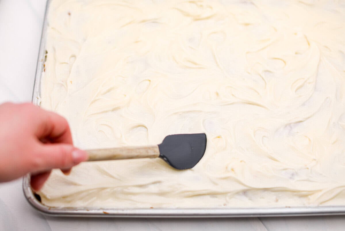 My carrot cake bars are so easy to make and unbelievably delicious. They are moist from the freshly grated carrots, perfectly spiced, and topped with an incredibly fluffy cream cheese frosting. Someone spreading the frosting over the carrot cake bars.