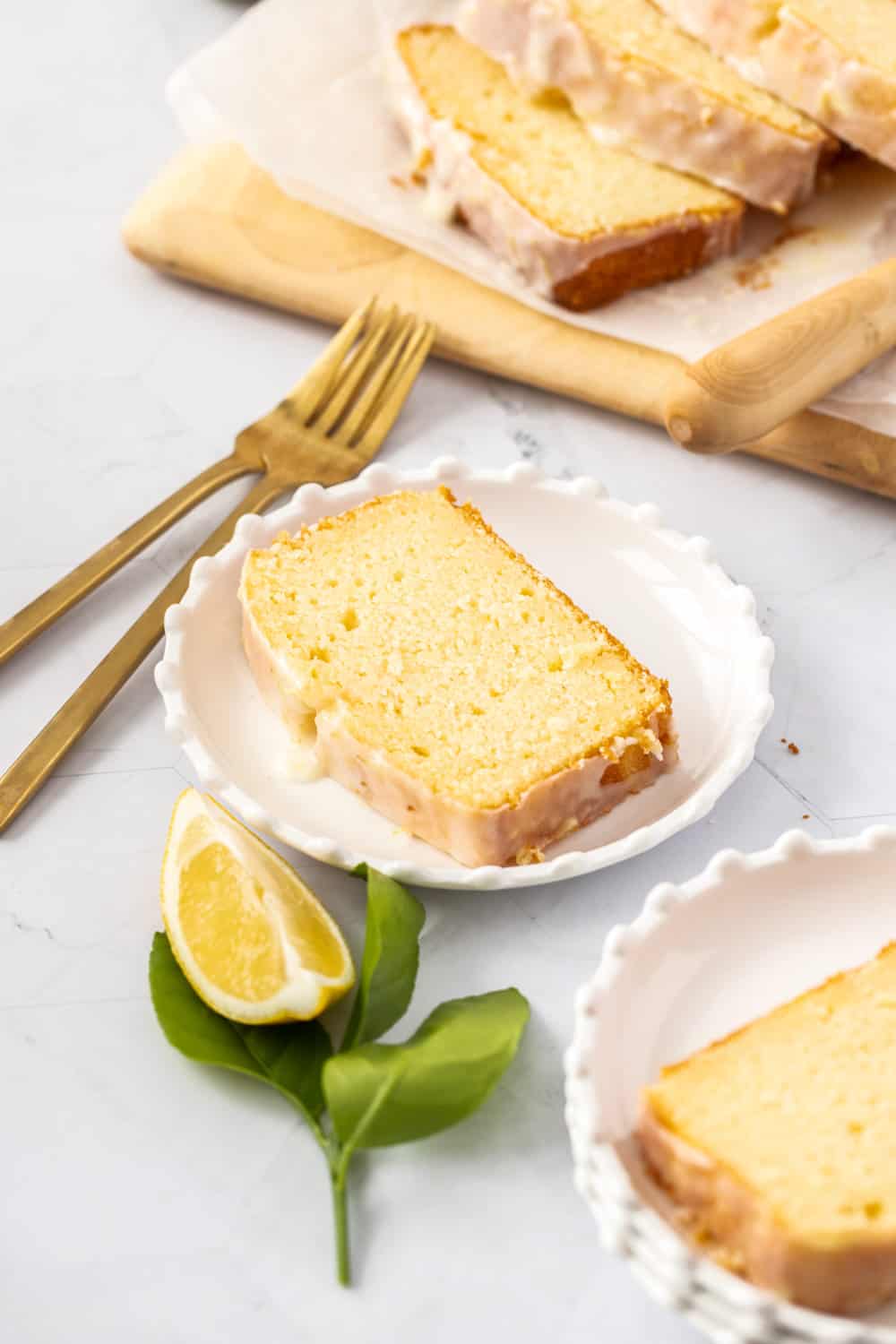 This bright and zesty glazed lemon pound cake is buttery, soft and topped with an easy lemon glaze. It is perfect for lemon lovers! A slice of cake on a white plate with gold fork nearby.
