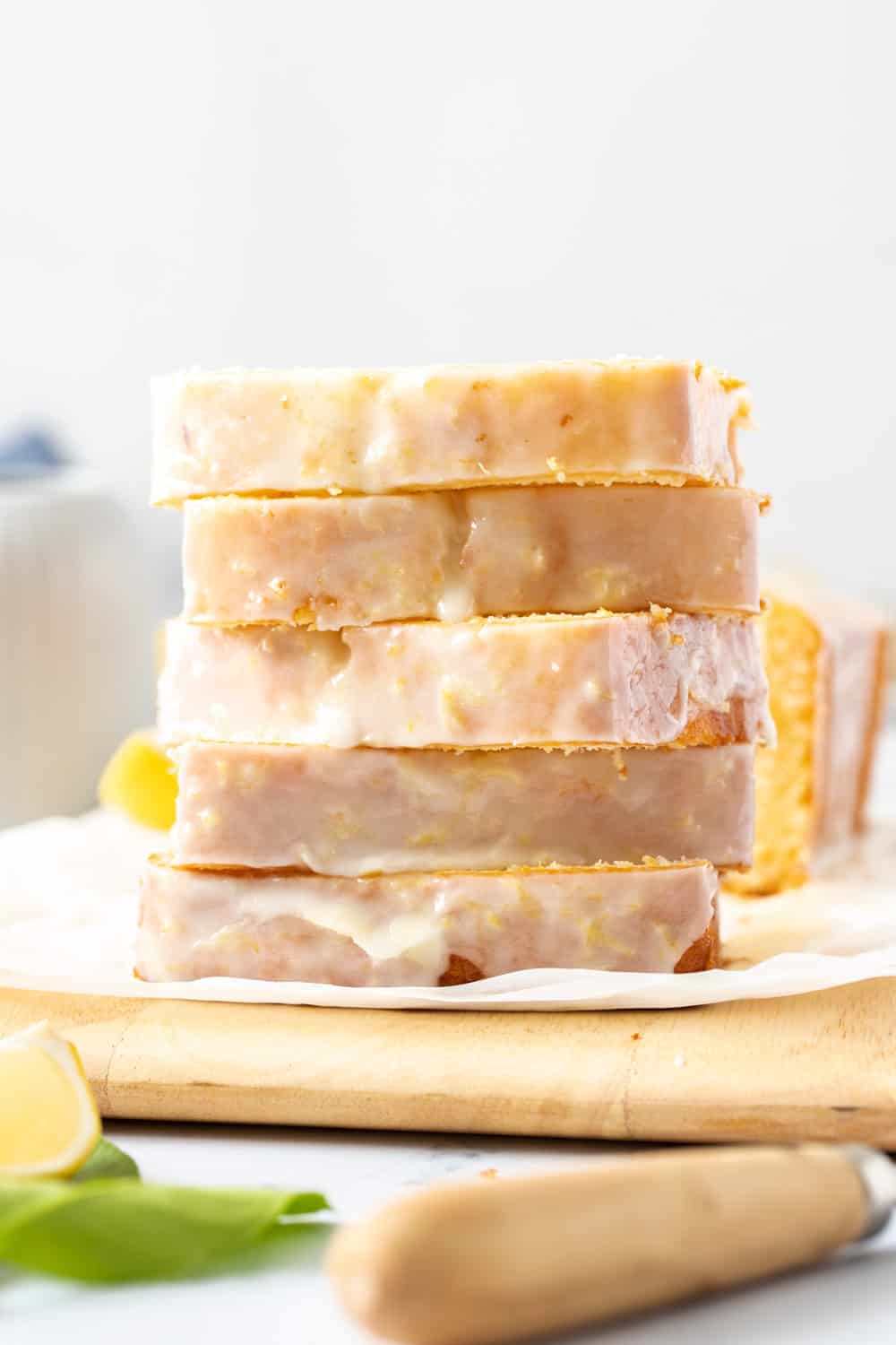 This bright and zesty glazed lemon pound cake is buttery, soft and topped with an easy lemon glaze. It is perfect for lemon lovers! A stack of flat cake slices on a wooden board.