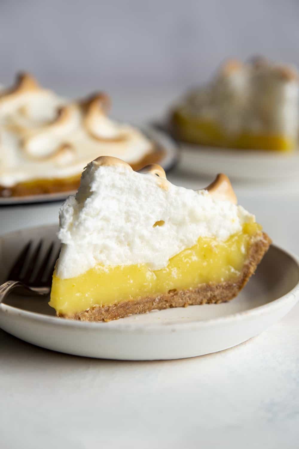 Lemon Meringue Pie is literally a slice of sunshine! Tart and tangy, bright lemon filling is topped with clouds of fluffy meringue that is going to blow your taste buds. Slice of Lemon Meringue pie on a plate.