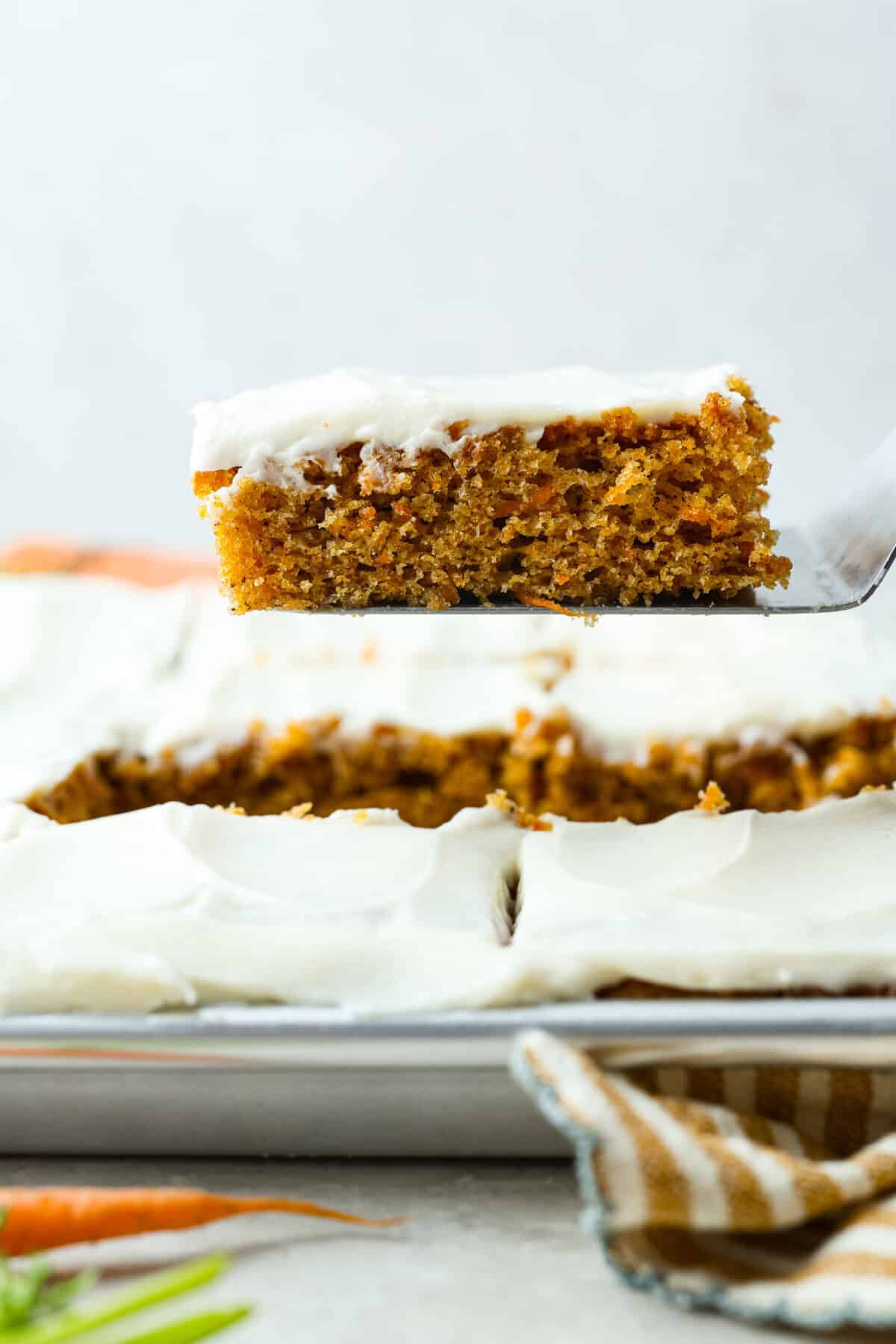 You have to try my insanely delicious Carrot Cake Bars! They’re easy to make, incredibly moist, perfectly spiced, and topped with fluffy cream cheese frosting! Side shot of someone lifting a carrot cake bar out of the pan.