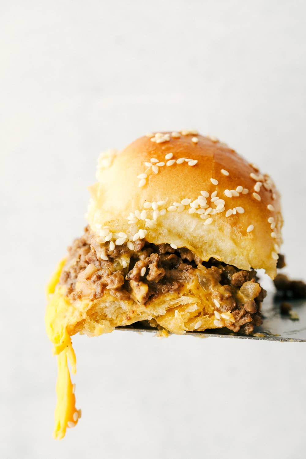 Cheeseburger Sliders are the best thing to happen to rolls since butter! These are fast, easy, and absolutely delicious. A single slider on a spatula with cheese dripping off.