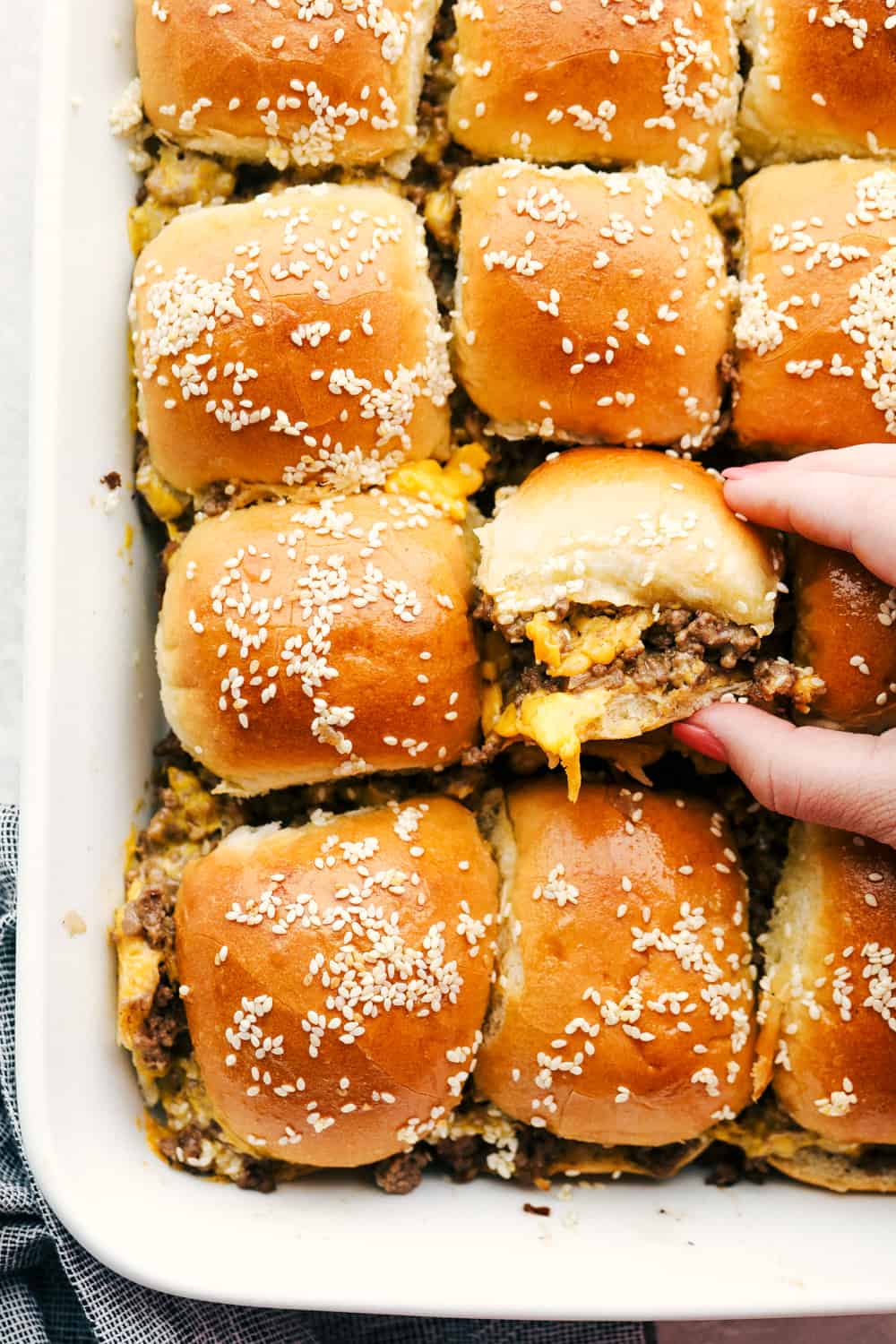 Cheeseburger Sliders are the best thing to happen to rolls since butter! These are fast, easy, and absolutely delicious. Grabbing a cheeseburger slider out of the pan.
