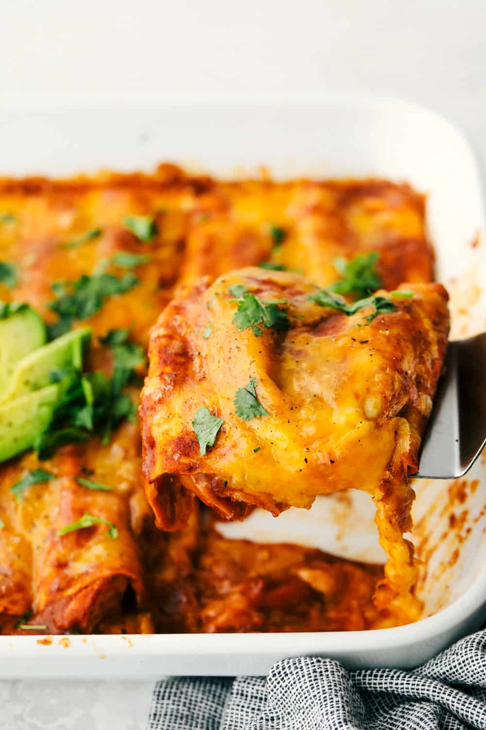 Chicken Enchiladas are saucy, cheesy and super scrumptious. These are made with my Enchilada sauce, which makes them even better than store bought! Scooping saucy chicken filled tortillas out of the pan.