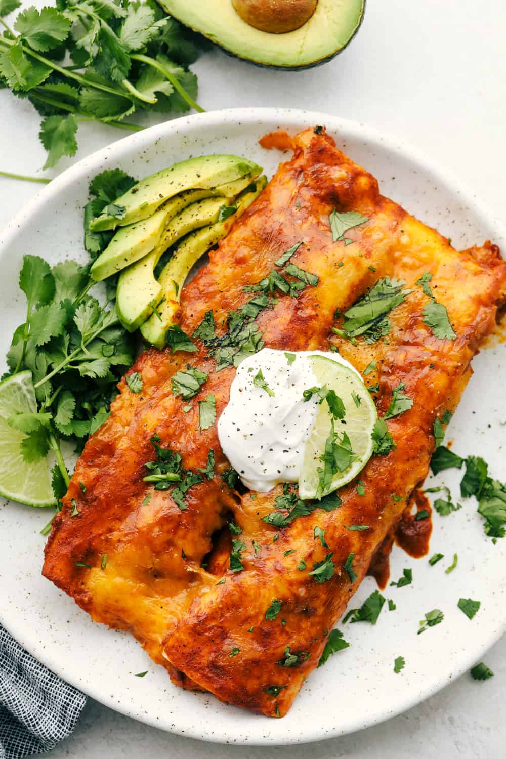 Chicken Enchiladas are saucy, cheesy and super scrumptious. These are made with my Enchilada sauce, which makes them even better than store bought! Enchiladas on a plate with sour cream and sliced avocados.