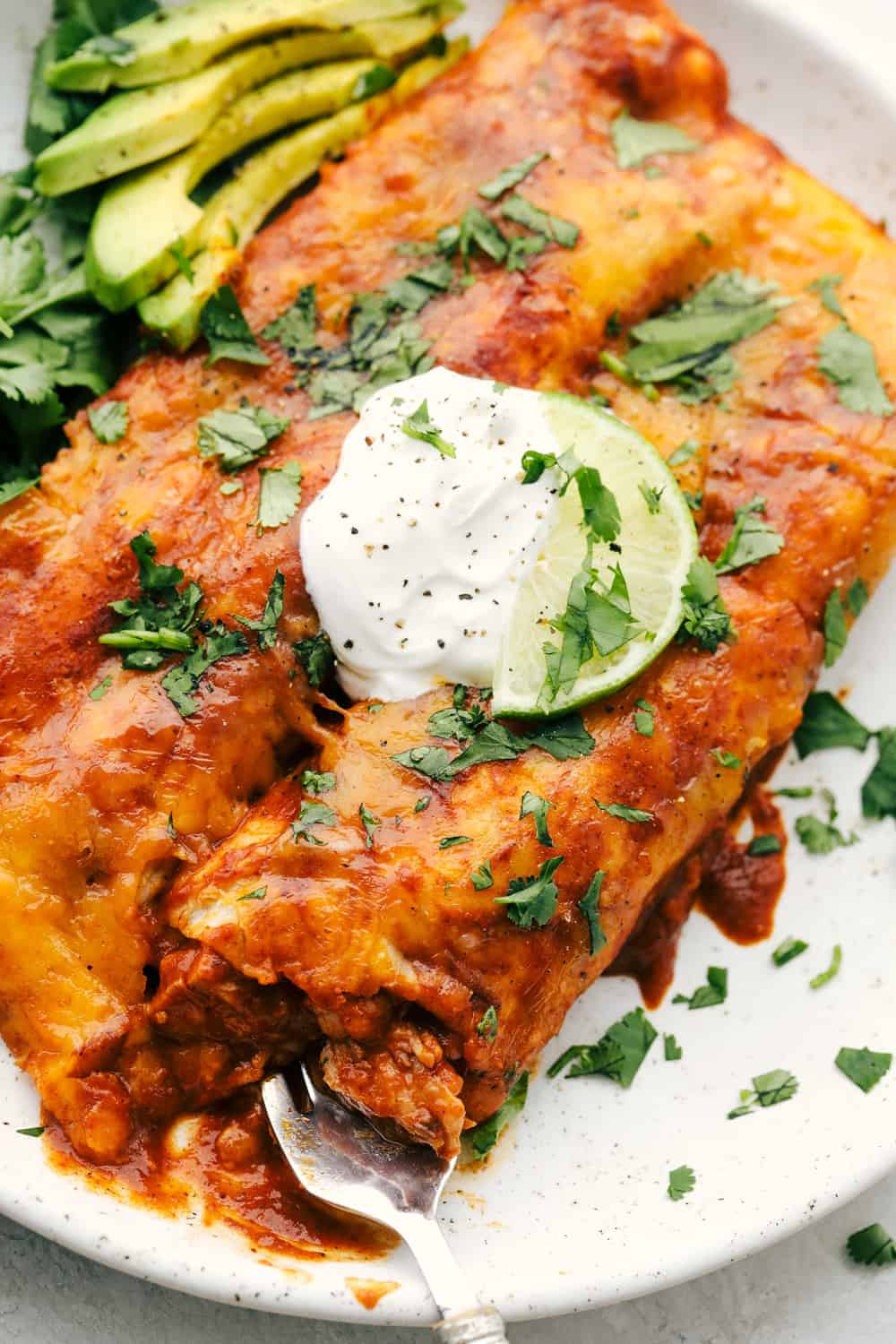 Chicken Enchiladas are saucy, cheesy and super scrumptious. These are made with my Enchilada sauce, which makes them even better than store bought! Showing a close up with a bite out one of them with a fork.