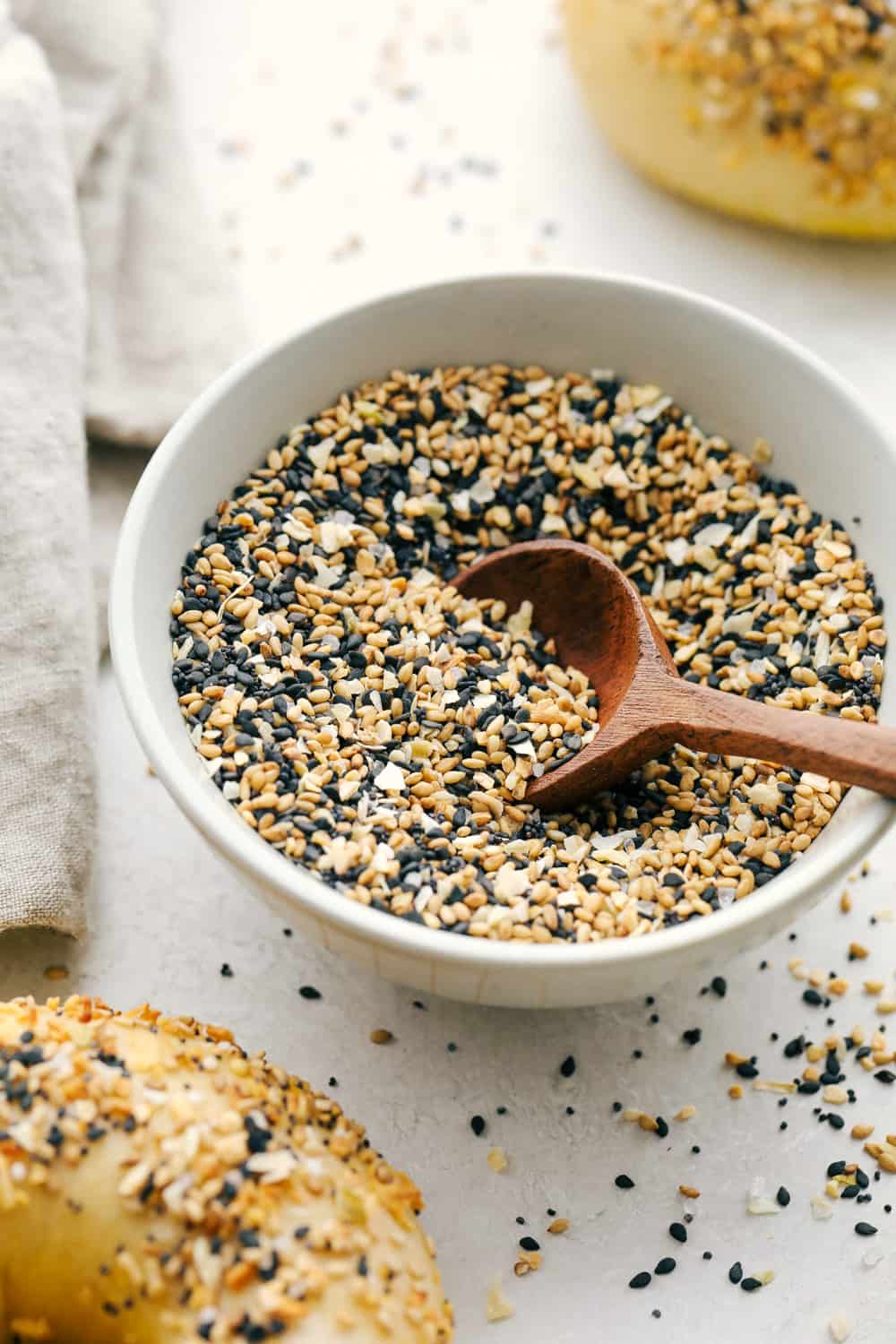 Everything Bagel Seasoning made at home takes 6 ingredients and less than 5 minutes! You are going to love this super easy and fast divine seasoning. A Bowl full of Everything but the bagel seasoning next to bagels.