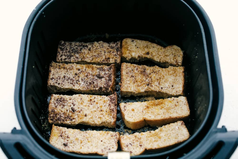 Air Fryer French Toast Sticks are a super fun fast way to make breakfast in the morning. Coated in a vanilla and cinnamon egg mixture, these fry up absolutely amazing! Placing french toast sticks in air fryer basket.