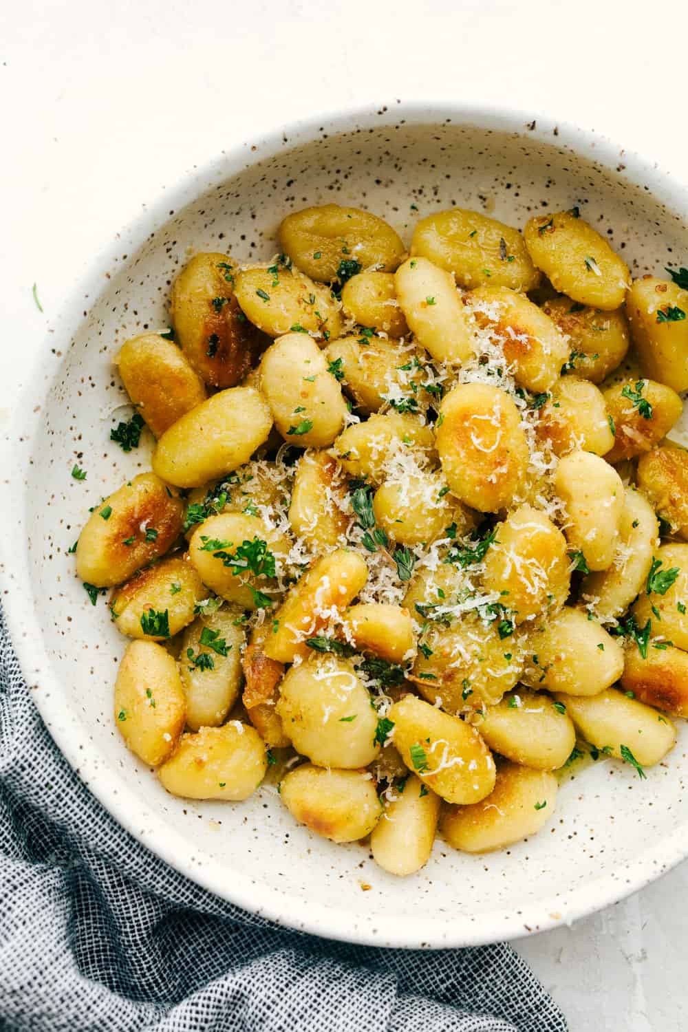 Brown Butter Garlic Fried Gnocchi are tender morsels tossed in a buttery herb sauce you are going to love! Super easy and quick, this is a perfect dish for busy nights or unexpected guests! Fried gnocchi with browned butter in a bowl and parmesan cheese.