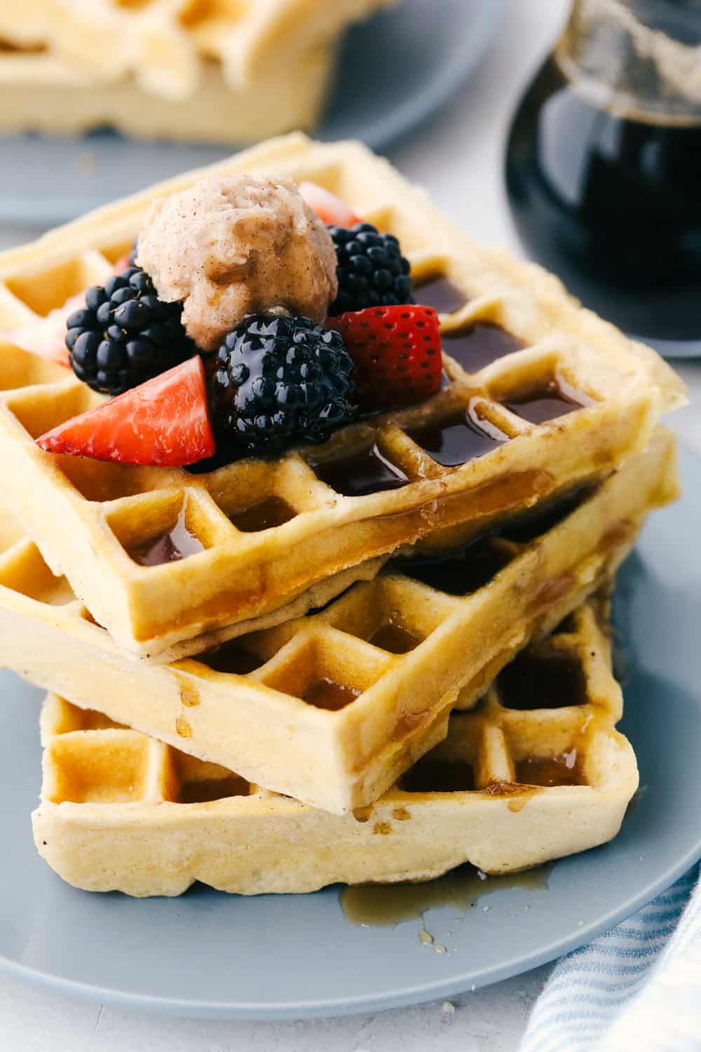 Homemade Waffles are worth waking up for! These delicate, crisp, yet fluffy waffles will melt in your mouth! A Stack of fluffy waffles with fruit and syrup on a plate.