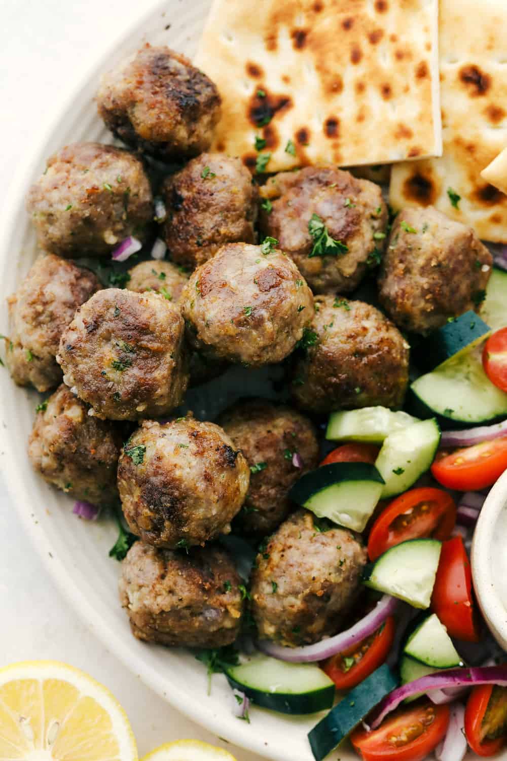 Greek Meatballs also known as Keftedes, are full of flavor and super delicious. These have all the greek flavor and super easy to make! Browned meatballs on a platter with pitas and vegetables.