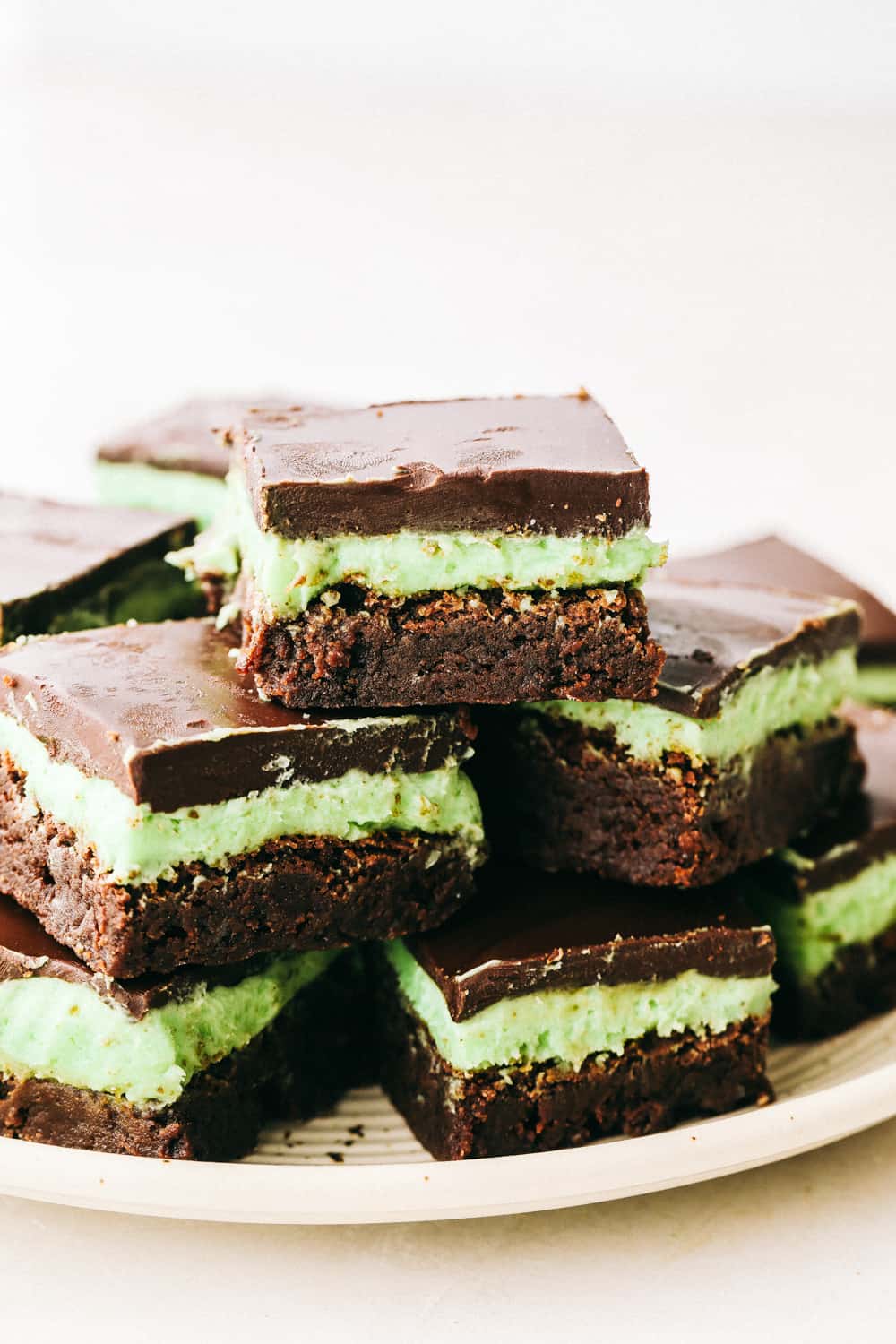 These are the Absolute Best Mint Brownies Ever! They have a thick fudgy brownie bottom, soft mint middle and a smooth, melt in your mouth ganache top! Layered mint brownies stacked on a white plate.