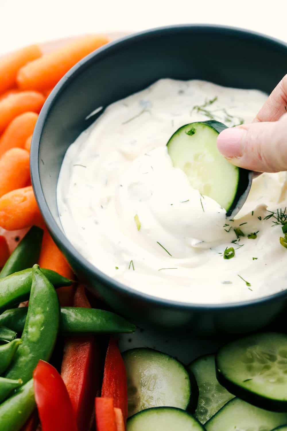 This Veggie Dip is easy, quick and the yummiest dip! This creamy, full of flavor dip is the perfect way to get your kids to eat their vegetables! Dipping a cucumber in the dip.