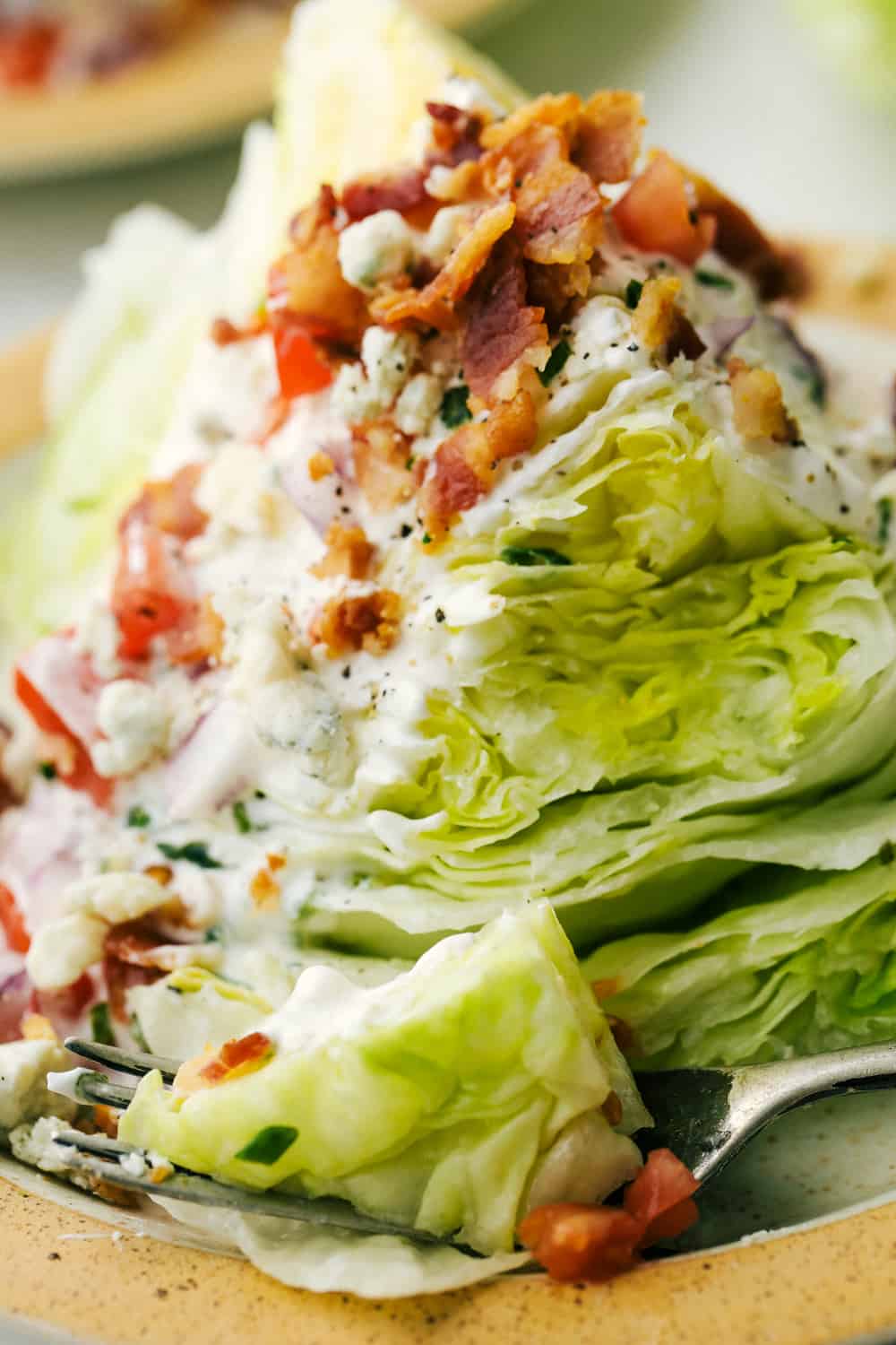 This classic wedge salad brings all the steakhouse vibes! Piled high with crispy bacon, fresh tomatoes, and a drizzle of creamy blue cheese dressing, it's a simple side that goes with just about anything. Up close picture of a wedge salad on a plate with a fork.