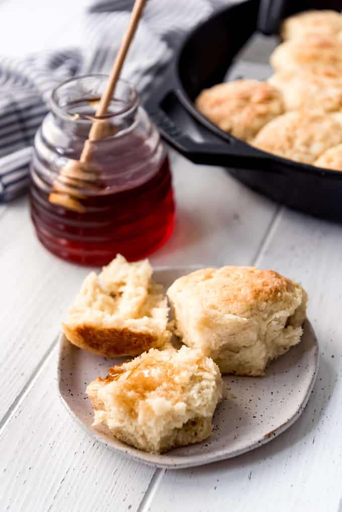 Angel Biscuits are a heavenly addition to any dinner table! These light and fluffy southern biscuits are quick and easy to throw together and they freeze great if you want to make them ahead! a biscuit on a plate with honey on it