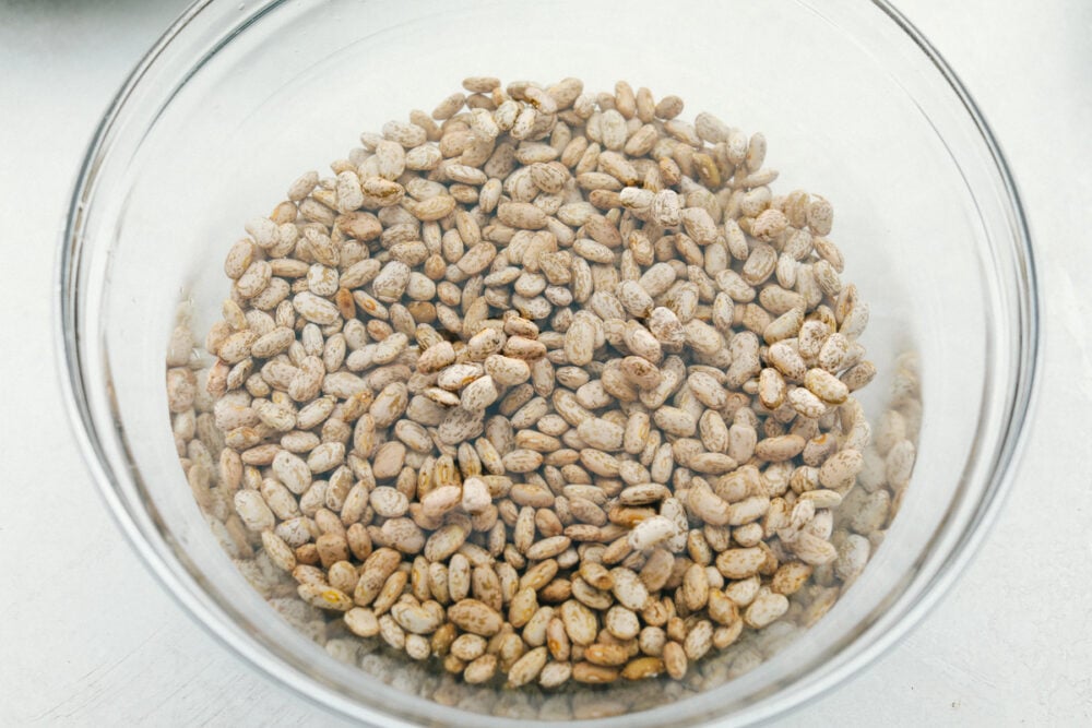 Homemade Refried Beans are simple and packed with so much flavor, you will never reach for a can again. These creamy refried beans are perfect for your next Tex-Mex night! Soaking dried beans in a glass bowl.