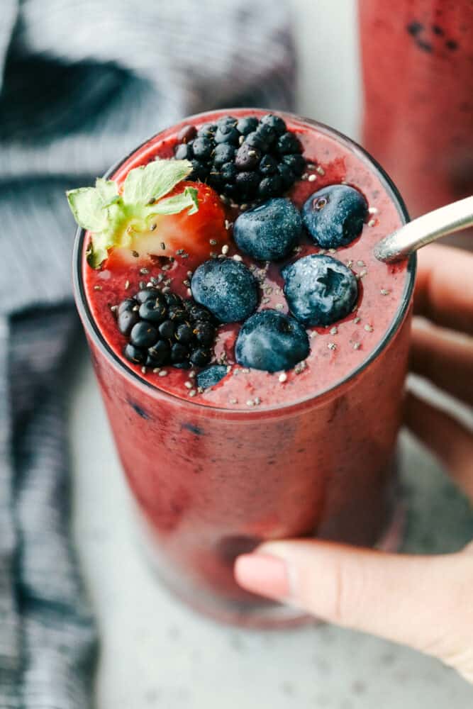 Mixed Berry smoothie is the perfect answer to the need for a quick healthy breakfast or snack. Packed with flavorful fruit, protein-filled Greek yogurt and honey, it's a family pleaser for sure! Holding a glass of berry smoothie getting ready to drink.