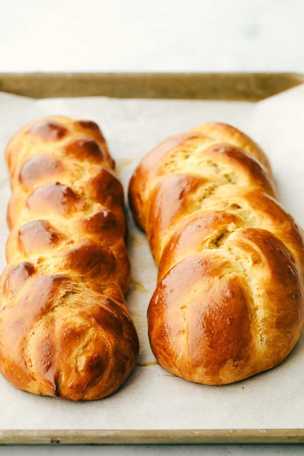 Challah Bread is a rich and fluffy loaf full of flavor. A Jewish traditional loaf, this incredible bread is going to be a favorite in your family baking! Two baked loaves of Challah golden brown.