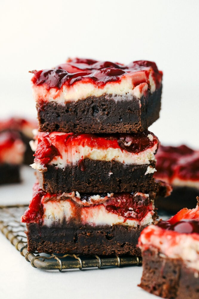 Cherry cheesecake brownies are fudgy brownies with cheesecake and premium cherry pie filling swirled on top! These brownies are rich and creamy and have three delicious desserts in one! Cherry Cheesecake brownies stacked on top of each other.