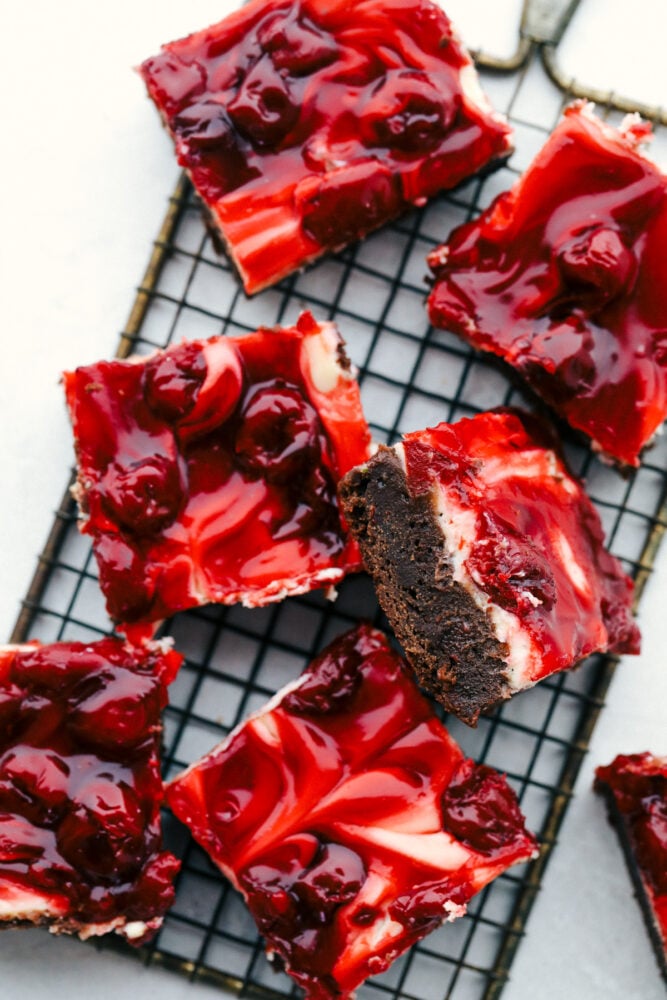 Cherry cheesecake brownies are fudgy brownies with cheesecake and premium cherry pie filling swirled on top! These brownies are rich and creamy and have three delicious desserts in one! Sliced Cherry cheesecake brownies on a cooling rack.