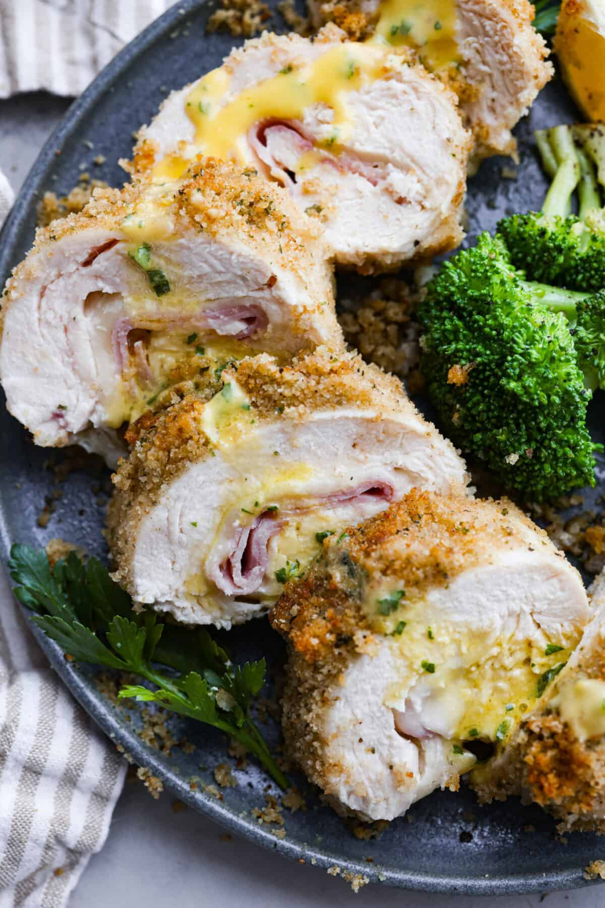 Chicken cordon bleu has a delicious layer of ham and cheese wrapped inside succulent crumb-coated chicken breast. Drizzled with mustard cream sauce, this oven-baked chicken is a classic French recipe your family will love! Close up shot of plated chicken cordon bleu.