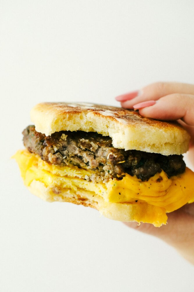 Homemade English Muffin Breakfast Sandwiches are the best thing to happen to your mornings! These are super easy, freezer friendly, and absolutely delicious! Holding an English muffin sandwich with a bite out of it.