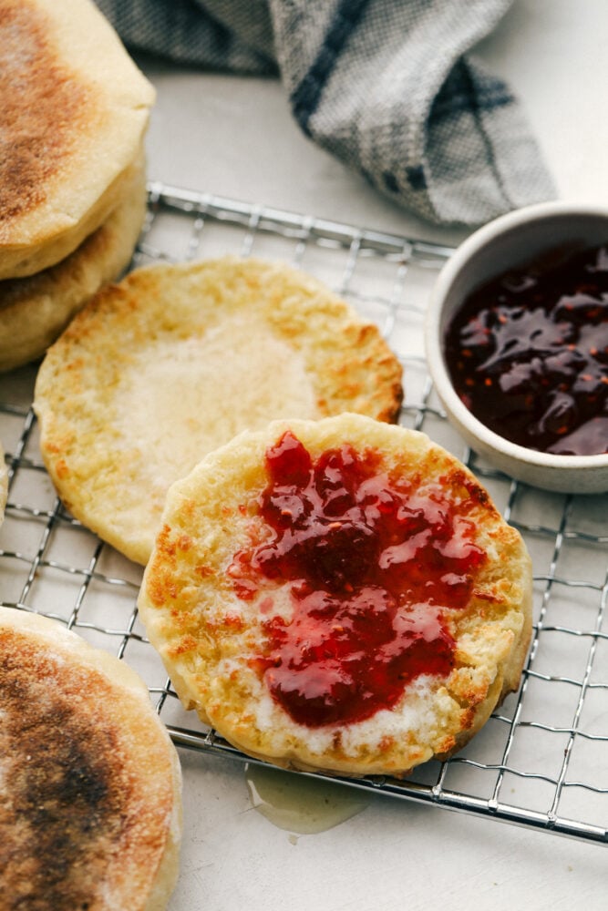 English Muffins are soft pillowy round morsels of absolute heaven. This is such an easy recipe you will be making them on a weekly basis! Toasted english muffins on a cooling rack with butter and jam.