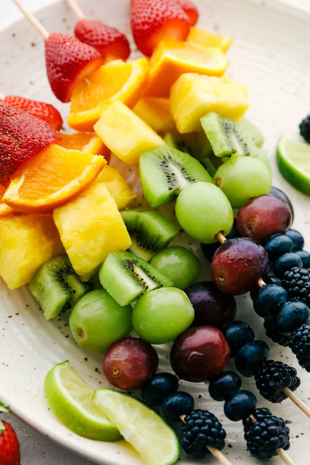 Fresh Rainbow Fruit Skewers are a super easy and fun sweet treat. Fruit skewers are a colorful, fun and yummy way to eat the recommended servings of fruit! Kabobs ready to eat on a plate.