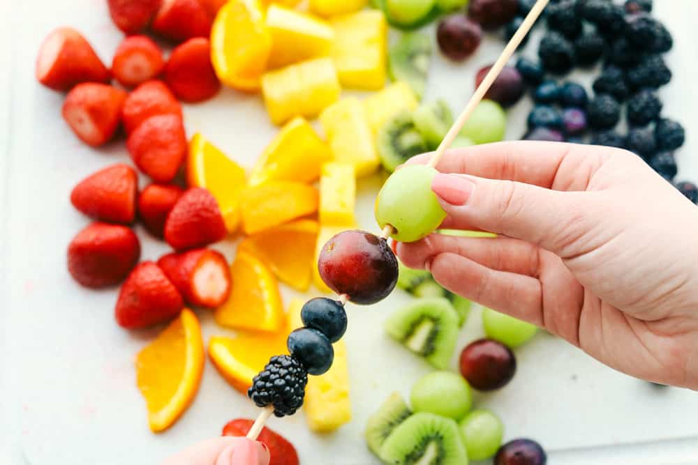 Fresh Rainbow Fruit Skewers are a super easy and fun sweet treat. Fruit skewers are a colorful, fun and yummy way to eat the recommended servings of fruit! Assembling the fruit on wooden skewers.