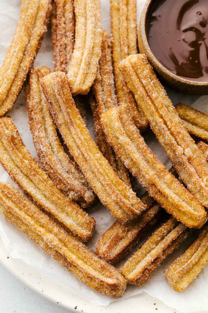 All I have to hear is the word, Churros, and my mouth starts to water. Light fluffy dough is fried and then covered in cinnamon and sugar, totally heavenly! A pile of fried churros with a side of chocolate dipping sauce.