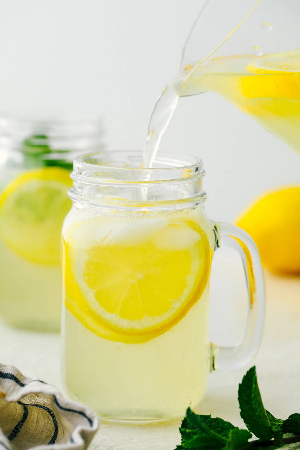 There isn't anything quite as refreshing as this Homemade Lemonade recipe, it's the BEST! Summer is going to be so cool, with a glass of this by your side. Pouring lemonade in glass mason serving jars.