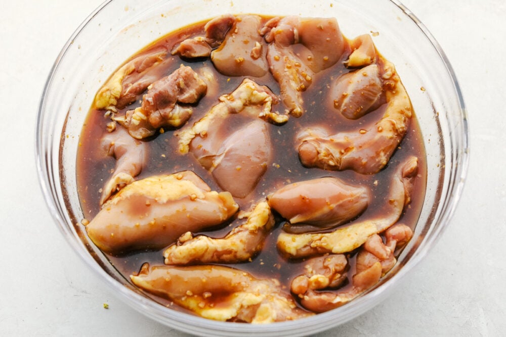 Grilled Huli Huli Chicken is a five star recipe! The marinade is quick and easy and full of such amazing flavor! You will make this again and again! Chicken thighs sitting in a bowl of marinade.