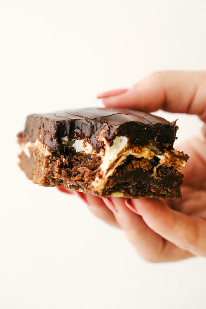 Mississippi Mudslide Bars are a chewy brownie base, topped with a fluffy marshmallow layer, and finished off with a rich and silky chocolate frosting. They are so addictive! My hand holding a mudslide bar.
