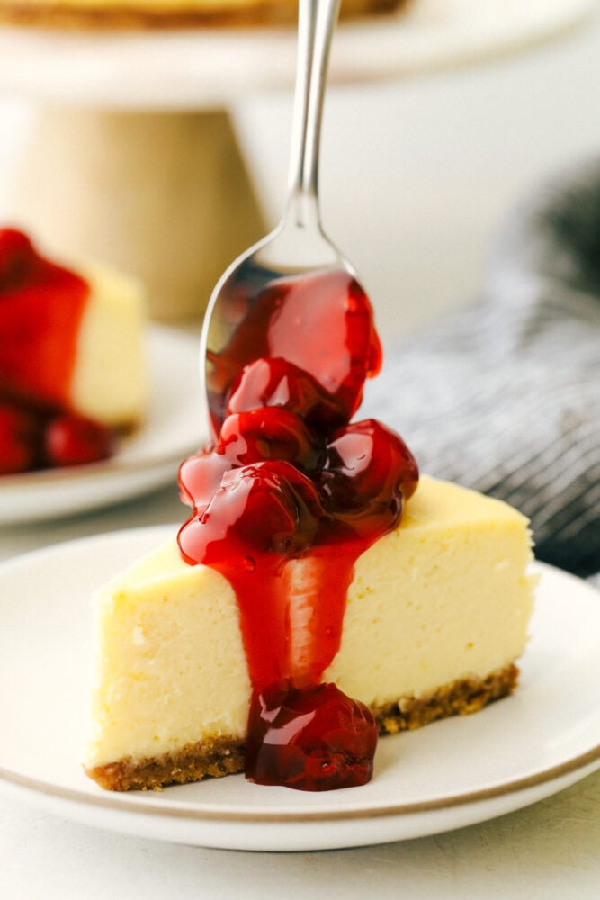 New York Cheesecake is a smooth, creamy dessert that is decant and always a favorite! This is an easy cheesecake that anyone can make. Cherries being put on top of the cheesecake.