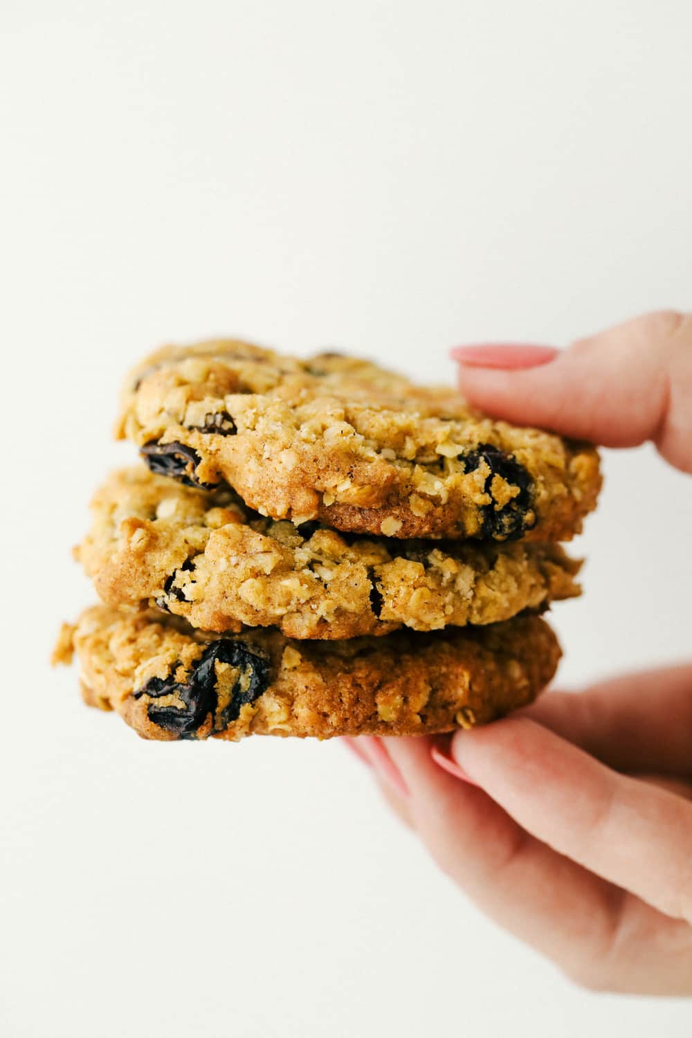 These are the Best Oatmeal Raisin Cookies you will ever make! These cookies are chewy, sweet and the perfect treat. Holding a stack of three cookies.