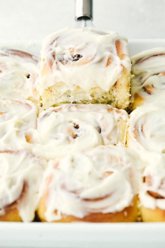 Overnight Cinnamon Rolls is a recipe you need in your arsenal. They make waking up worth it in the morning! Scooping a cinnamon roll out of the pan.