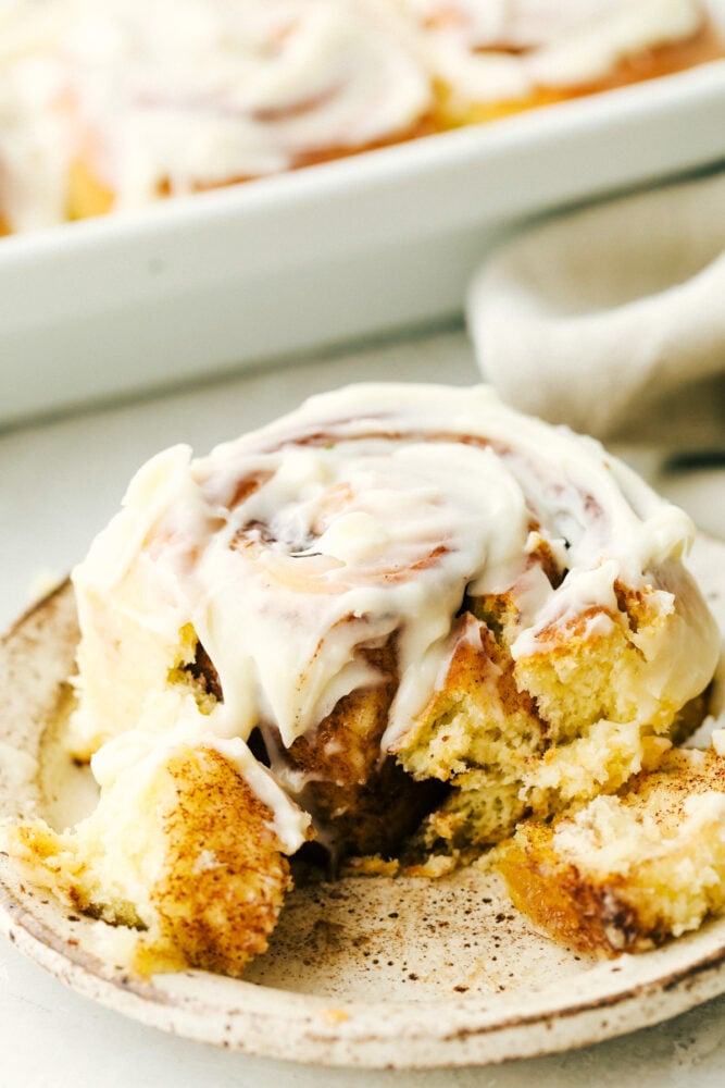 Overnight Cinnamon Rolls is a recipe you need in your arsenal. They make waking up worth it in the morning! Cinnamon roll on a plate half eaten.