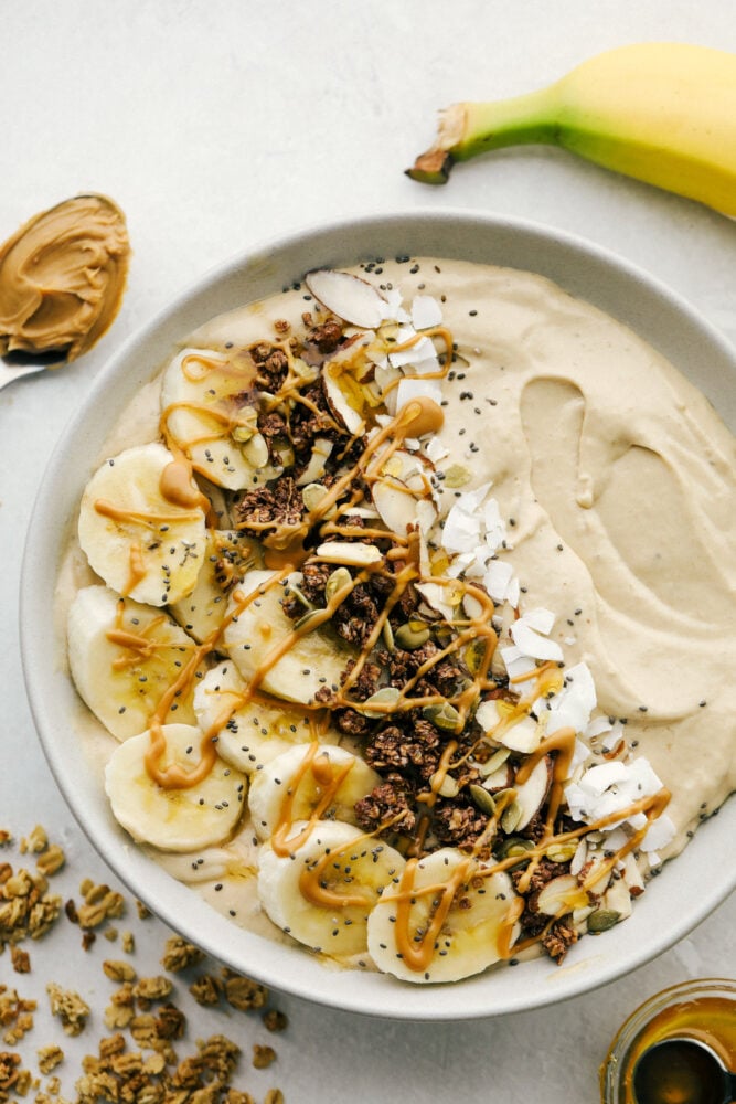 Peanut Butter Smoothie Bowl is one of the best ways to get your protein in for the day! It tastes like you are eating luscious ice cream, only it's so much better for you Peanut butter smoothie bowl, topped with bananas, chocolate granola and nuts.