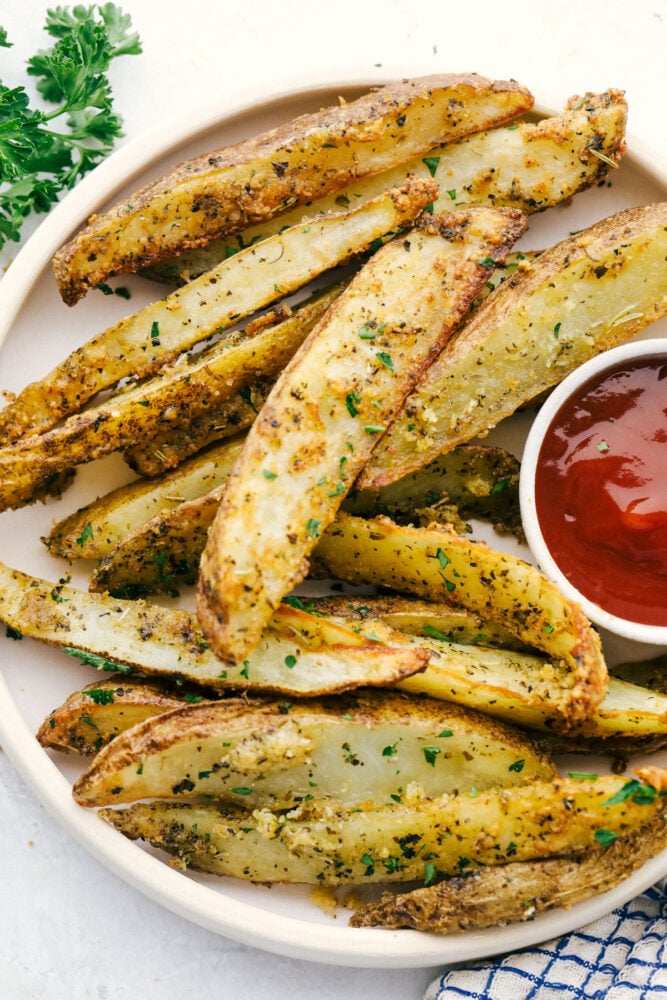 Air Fryer Potato Wedges are seasoned with a crispy outside and perfectly tender on the inside! These are so insanely delicious you are going to love them! Air Fryer potato wedges on a plate with ketchup.