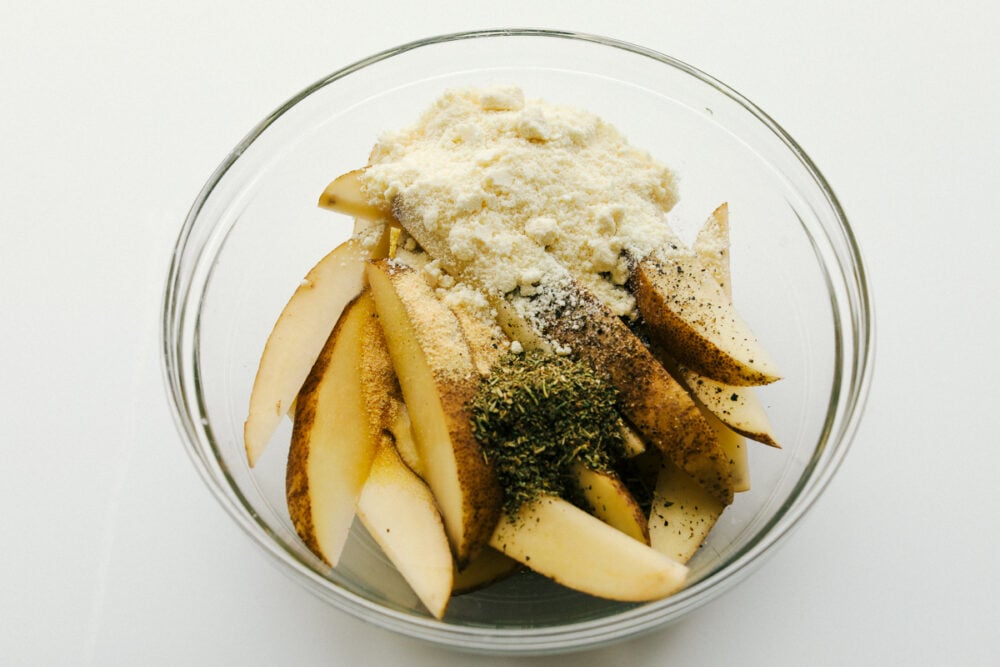 Air Fryer Potato Wedges are seasoned with a crispy outside and perfectly tender on the inside! These are so insanely delicious you are going to love them! Potato wedges in a bowl with seasonings.