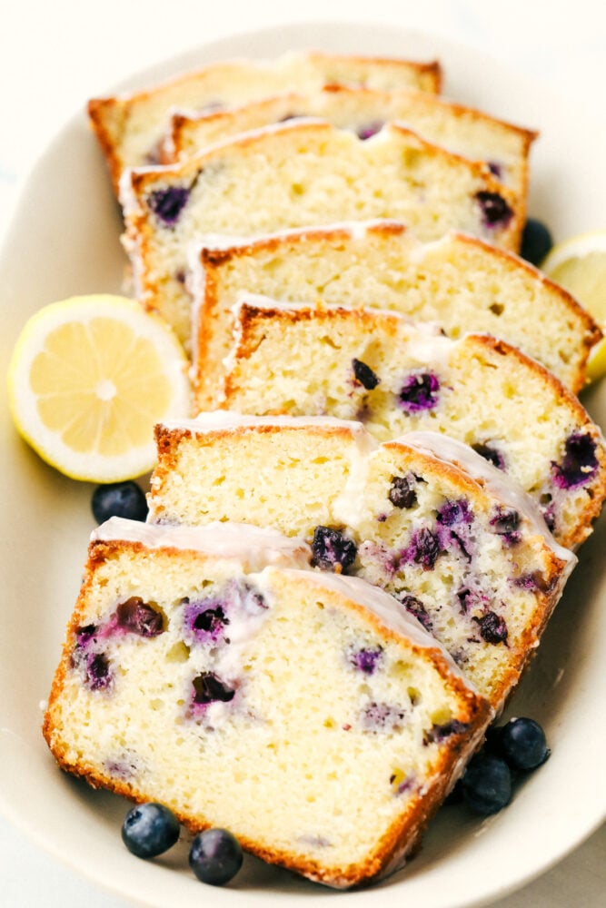 Blueberry Lemon Pound Cake! ย This pound cake is made lighter by using greek yogurt, and is loaded up with lemon flavor thanks to zest and fresh lemon juice! Juicy blueberries are baked right in. All drizzled with a luscious lemon glaze.ย Slices of the cake with lemon glaze on a plate.