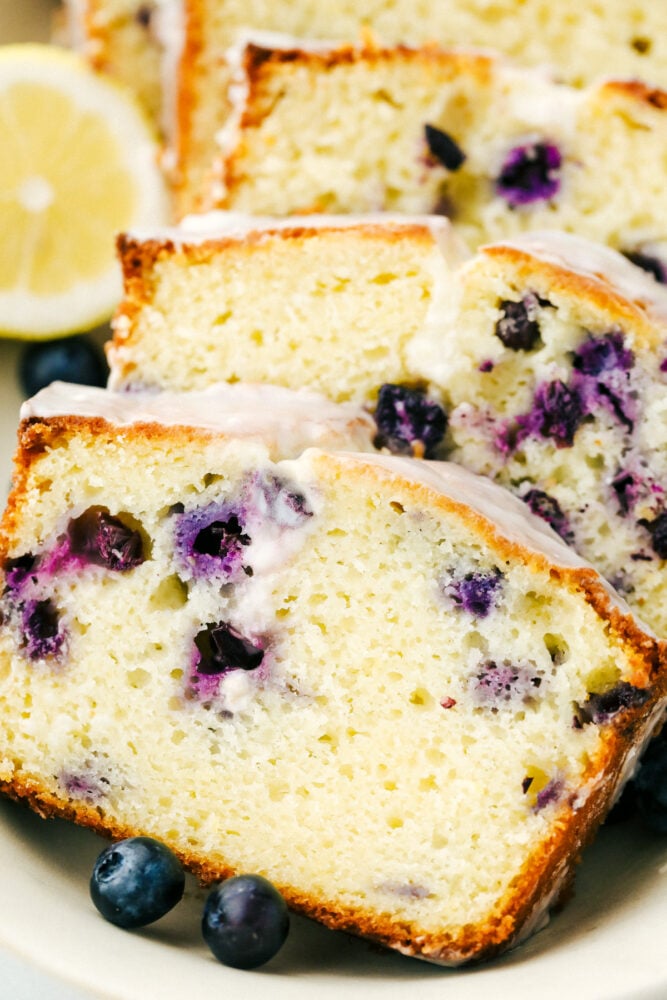 Blueberry Lemon Pound Cake is a pound cake made lighter by using greek yogurt, and is loaded up with lemon flavor thanks to zest and fresh lemon juice! Juicy blueberries are baked right in, then drizzled with a luscious lemon glaze. Sliced blueberry lemon pound cake on a plate.