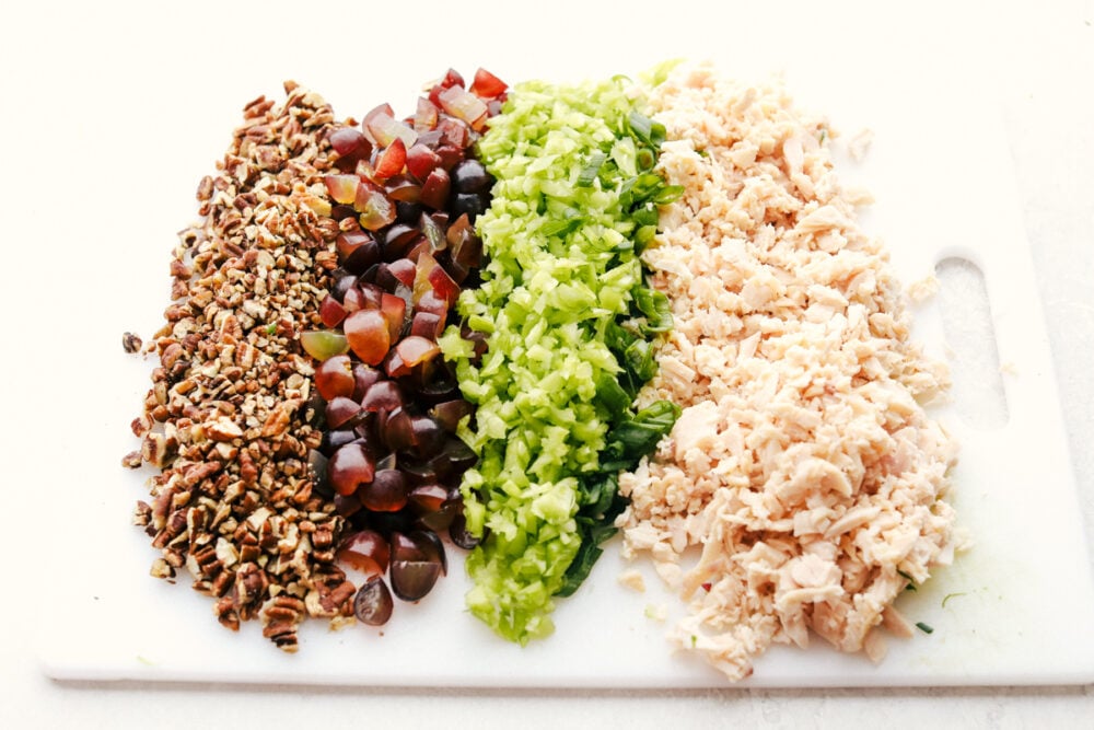 This is the Best Chicken Salad EVER! Perfect for summer picnics, festive lunches and anytime in between! Pecans, grapes, celery, onions and chicken on a cutting board.
