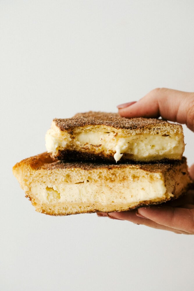 Holding two churro cheesecake bars.
