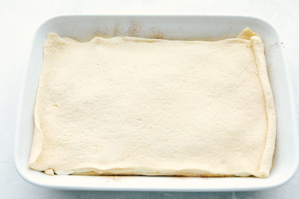 Layering the second sheet of cresent rolls over the cream cheese layer.