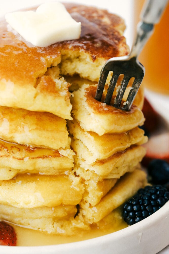 I am not joking when I say these are to die for Cornbread pancakes with honey butter syrup. These may well be the most amazing pancakes you will ever have! Using a fork to take a bite out of the stack of cornmeal pancakes.