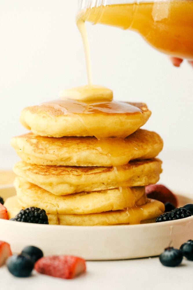 I am not joking when I say these are to die for Cornbread pancakes with honey butter syrup. These may well be the most amazing pancakes you will ever have! A stack of cornmeal pancakes with honey butter syrup being poured over the top.