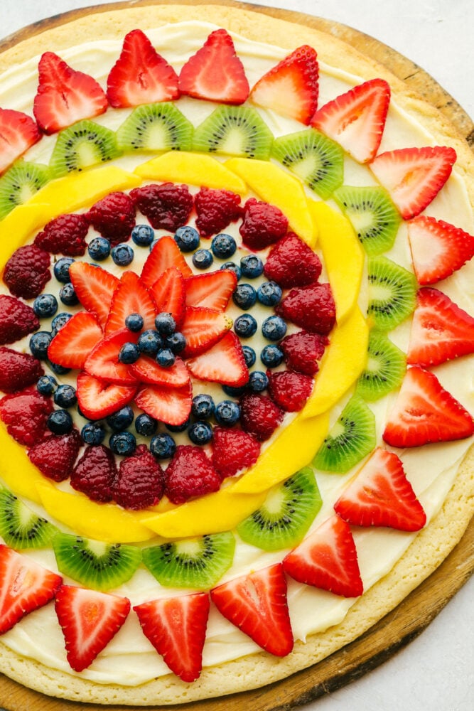 This Fruit Pizza is a sweet refreshing dessert that is always a hit! Full of color, and pizzaz this is a delicious way to eat your fruit! Fruit pizza with fresh fruit cut up and frosting underneath.